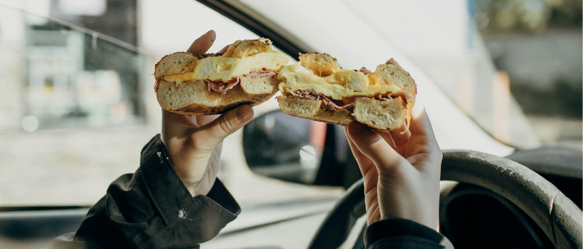 egg bagel sandwhich held inside of a car